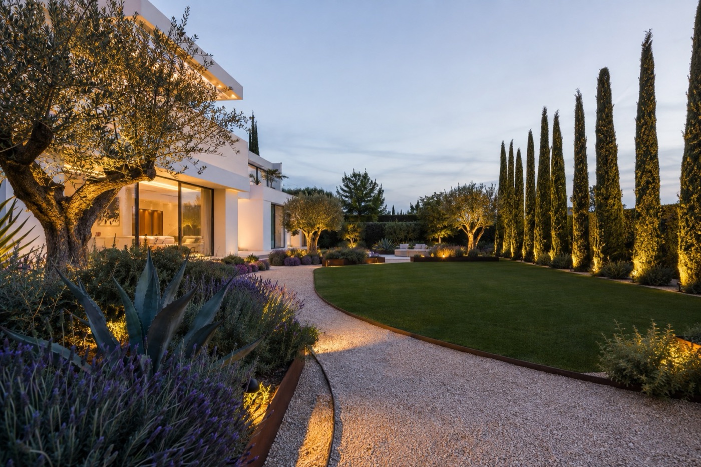 Jardín de una villa moderna con césped, cipreses y olivos al anochecer